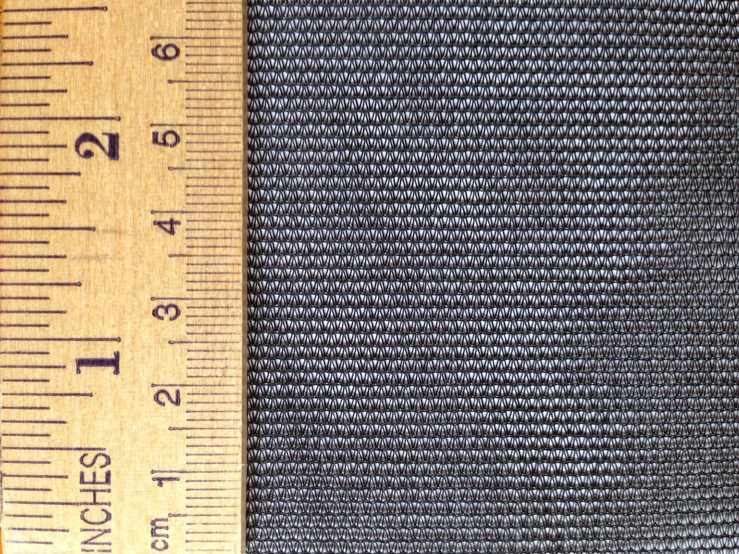 Close-up of a textured dark fabric alongside a wooden ruler, showing measurements. Useful for illustrating fabric characteristics in a textile context.