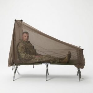 A soldier in camouflage clothing relaxes inside a mesh mosquito net, set up over a folding cot, highlighting camping or field readiness.