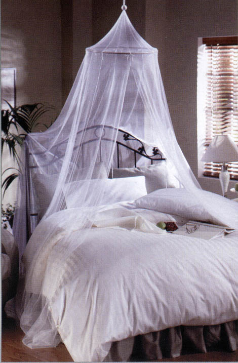 A canopy bed with a white mosquito net drapes over a neatly made bed, creating a serene and stylish sleeping space in a softly lit room.