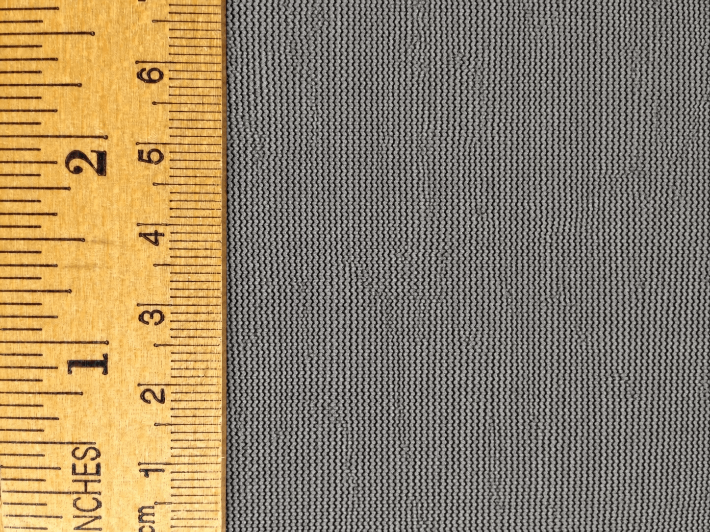 Gray fabric background with a wooden ruler measuring up to 6 inches, showcasing precise dimensions for textiles or crafts.
