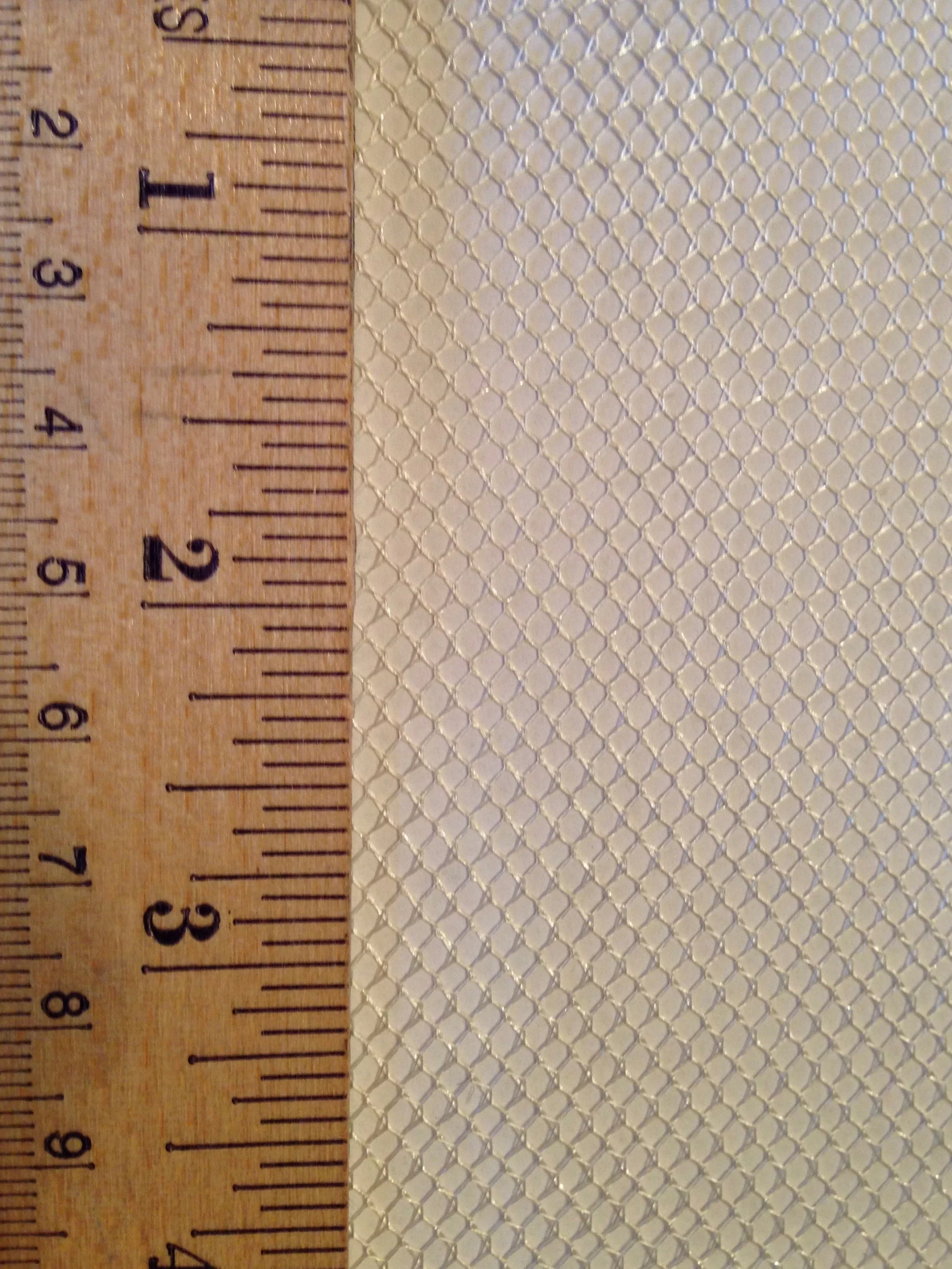 Close-up of a textured, hexagonal mesh material alongside a ruler measuring up to 3 inches, illustrating its size and pattern for textile reference.