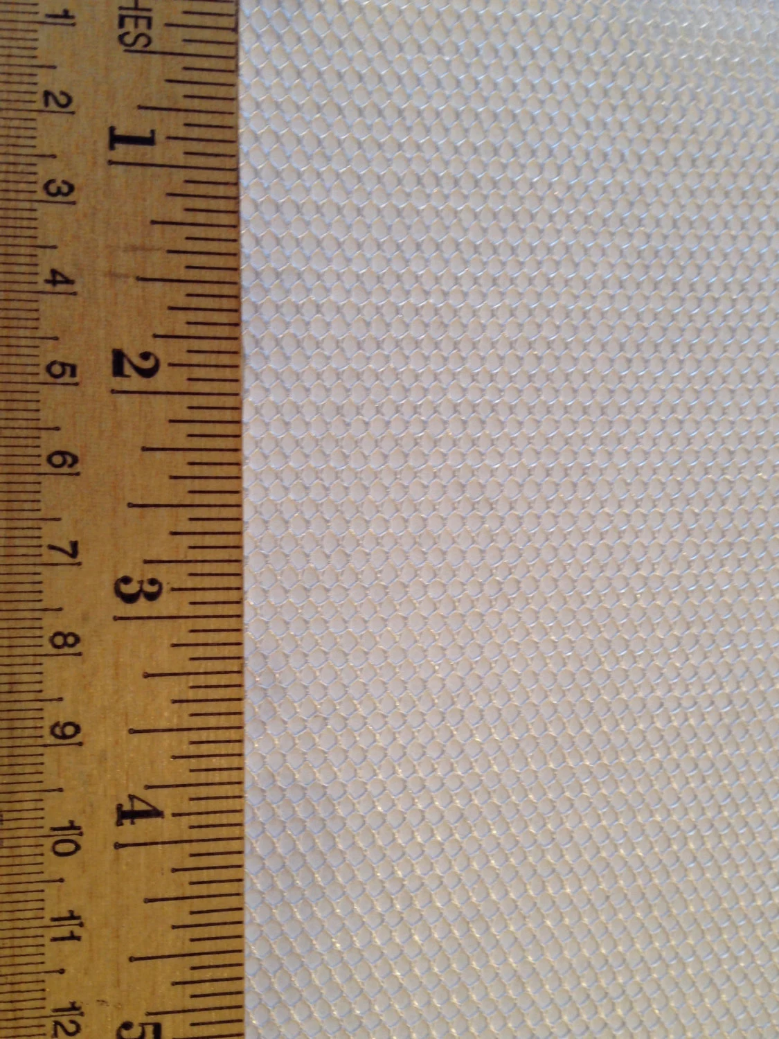 Close-up of a honeycomb-patterned material beside a wooden ruler, illustrating the texture and dimensions for crafting or design purposes.