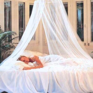 A woman peacefully sleeps under a sheer white canopy on a neatly made bed, surrounded by soft bedding and greenery, evoking tranquility and relaxation.