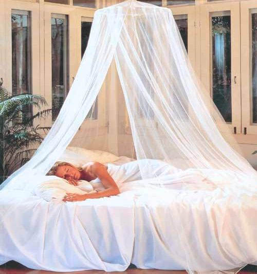 A woman peacefully sleeps under a sheer white canopy on a neatly made bed, surrounded by soft bedding and greenery, evoking tranquility and relaxation.